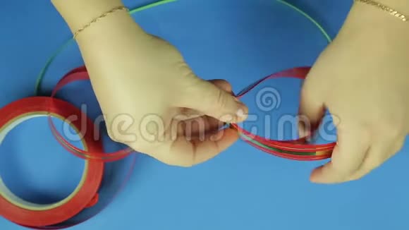 女性的手用剪刀剪角作为红色丝带礼物蝴蝶结蓝色背景视频的预览图