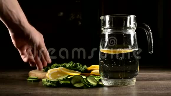 将柠檬黄瓜和薄荷叶切成薄片放在木切割板上旁边是一个带有起泡水的玻璃杯男性视频的预览图