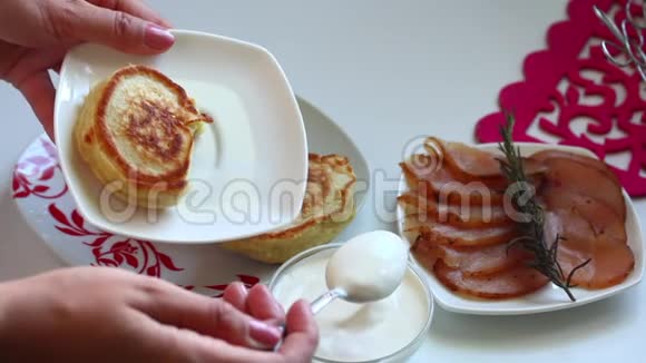 女人在盘子上的煎饼上加了酸奶油准备煎饼视频的预览图