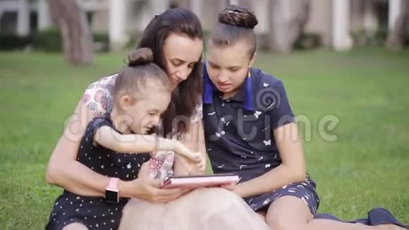 母女俩在草地上用药片妈妈在草地上给两个女儿读故事视频的预览图