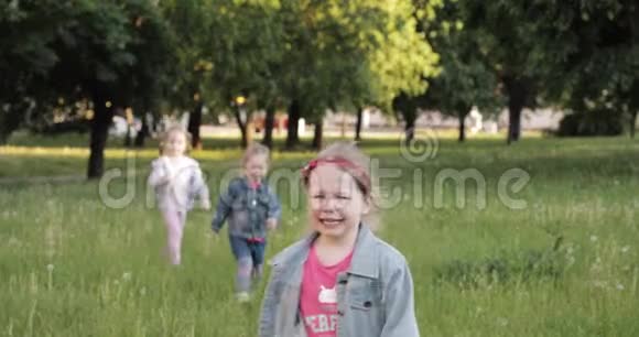 三个小女孩手牵着手在花园的绿草上奔跑周围是空气吹泡器视频的预览图