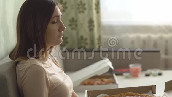 孤独悲伤的女孩带着披萨坐在家里的沙发上看电影视频的预览图