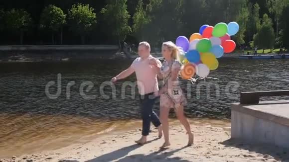 慢动作视频快乐的年轻夫妇拿着一大堆气球在海滩上奔跑视频的预览图