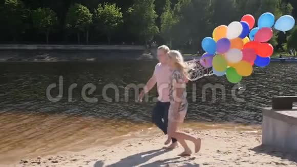 一对幸福的情侣在湖边用一大堆五颜六色的气球奔跑的慢动作视频视频的预览图