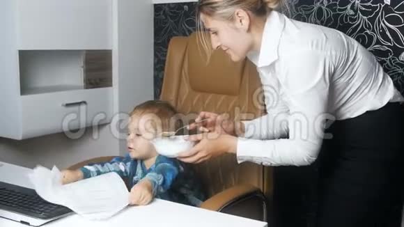 4K录像显示年轻女商人和她的孩子坐在办公室里试图给他喂汤视频的预览图
