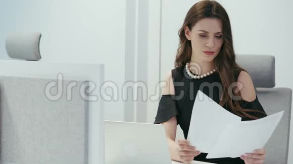 女商人坐在办公桌前拿着电脑和检查文件视频的预览图