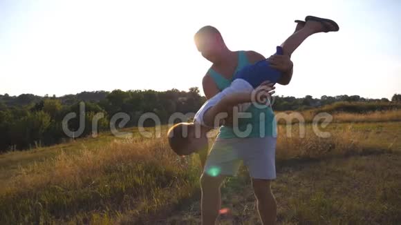 父亲和儿子在阳光明媚的夏日在田野上玩耍快乐的爸爸手里拿着他的孩子旋转男孩视频的预览图