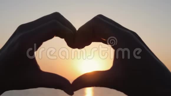 女性的双手特写在天空中的心脏形状通过太阳的光芒手的形状是爱的心在视频的预览图