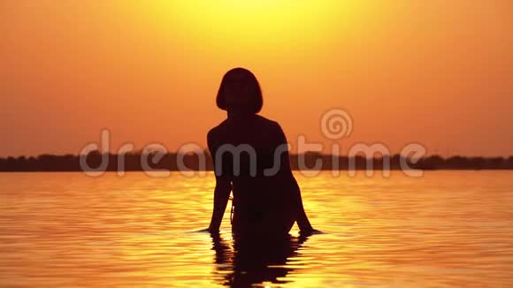 日落时的女人剪影举起双手创造水的飞溅慢动作视频的预览图