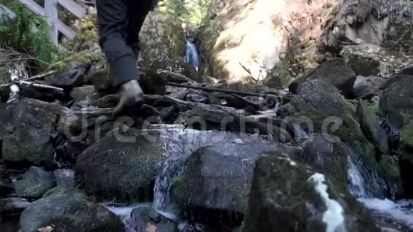 一个戴着帽子和白色夹克的人在小瀑布附近的山上旅行的后景录像高级官员视频的预览图