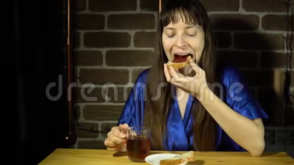 年轻女子正在吃一个夹有果酱的三明治喝茶视频的预览图