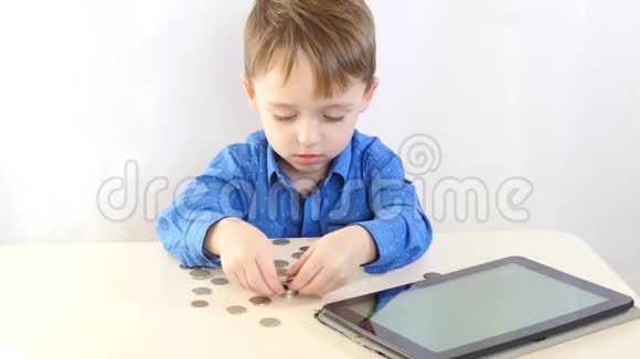 一个小男孩坐在一张桌子旁在白色的背景上用硬币玩他的手视频的预览图