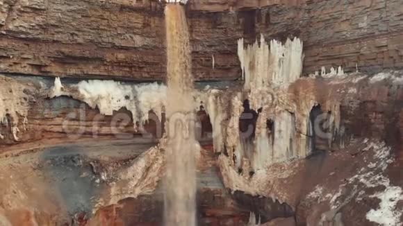 在覆盖着冰雪的棕色悬崖层上一条条棕色河流的水进入小瀑布视频的预览图