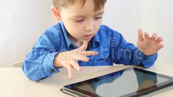 一个小男孩坐在桌子旁在平板电脑上玩这孩子正在喝茶视频的预览图
