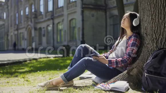 女学生坐在草地上靠在树上听音乐放松视频的预览图