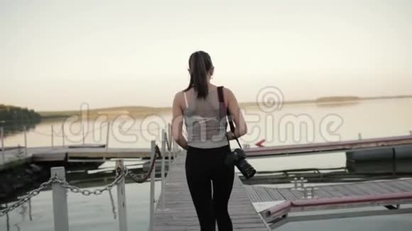 女孩带着相机走在湖边的码头上视频的预览图
