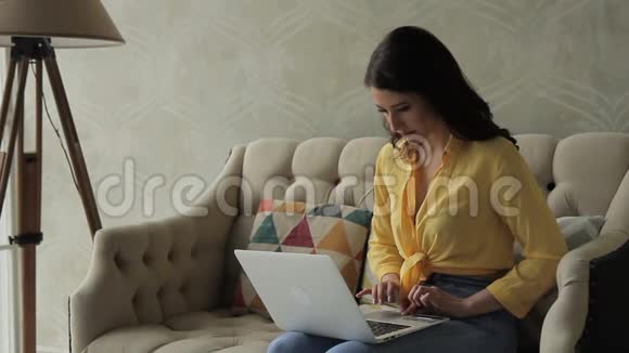 女人坐在沙发上膝盖上放着银色的笔记本电脑输入文字敲击键盘然后拿银行卡进入个人视频的预览图