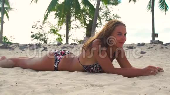 微笑的女人躺在沙滩上在暑假的时候晒日光浴快乐的女人在沙滩上晒太阳视频的预览图