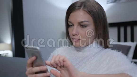 漂亮的女孩在卧室里坐着用智能手机视频的预览图