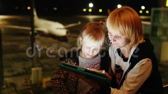 妈妈和女儿在机场玩平板电脑傍晚时分飞机在窗外可见视频的预览图