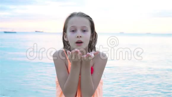 可爱的小女孩在海滩上玩得很开心快乐的孩子看着镜头背景美丽的天空视频的预览图