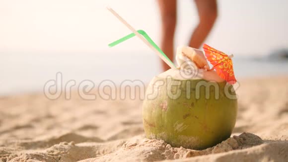 年轻的旅游女孩在热带海滩游泳后从沙滩上挑选美味的新鲜泰国椰子鸡尾酒4K视频的预览图