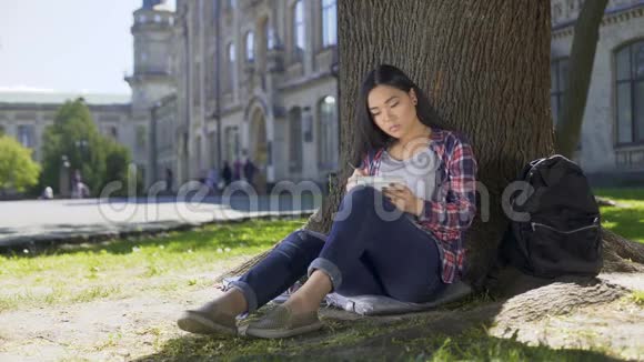 跨国青年妇女坐在树下写笔记写文章视频的预览图