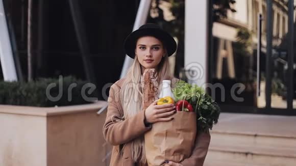 年轻漂亮的女人穿着时尚的外套站在街上拿着一包产品她拿着黄色的视频的预览图