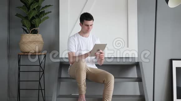男人坐在楼梯上浏览和滚动平板电脑视频的预览图