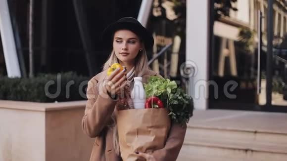 年轻漂亮的女人穿着时尚的外套站在街上拿着一包产品她拿着黄色的视频的预览图