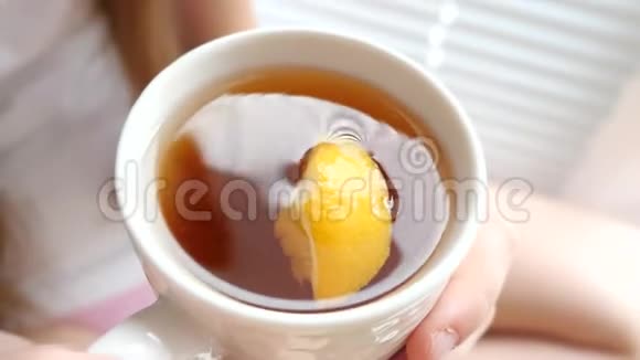 漂亮的女孩从杯子里喝热茶柠檬朝窗外看视频的预览图