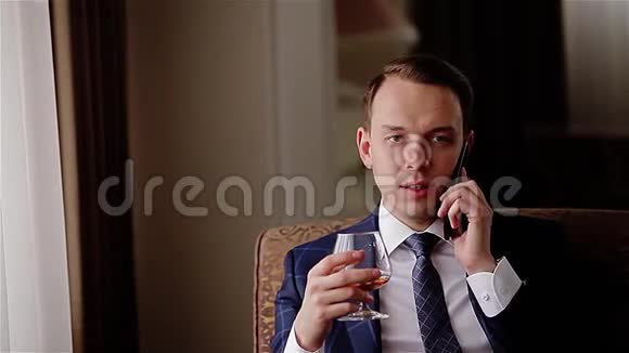 时髦的年轻人坐在沙发上打电话喝着杯子里的威士忌视频的预览图