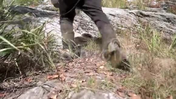 在荒草中的山上徒步旅行时把人的橡胶靴合上徒步旅行者的双腿攀登陡峭的山峰视频的预览图