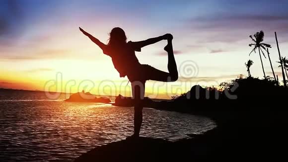 美丽的风景年轻女子做瑜伽伸展在岩石和海景日落慢动作视频的预览图