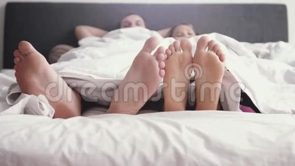 年轻可爱的快乐夫妇在毯子下玩耍而早上在床上醒来慢动作3840x2160视频的预览图