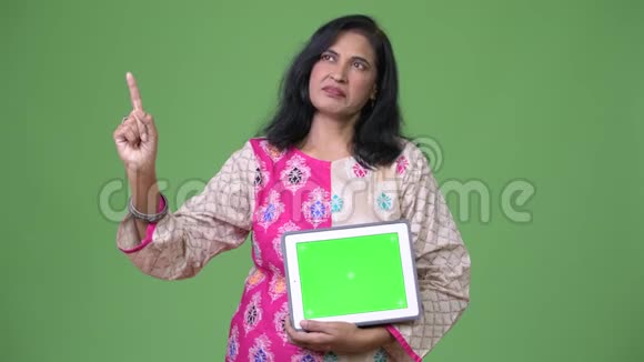 成熟美丽的印度女人一边看着数码平板电脑一边指着手指视频的预览图