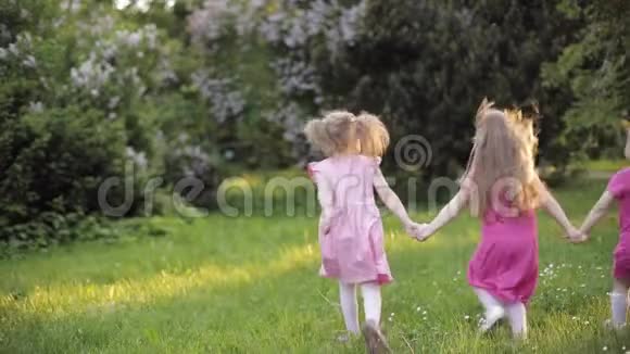 三个小女孩手牵着手在花园的绿草上奔跑周围是空气吹泡器视频的预览图
