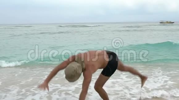 年轻的运动适合英俊的男人在海滩上快乐地跳跃制作轮子一些乐趣暑假的概念视频的预览图