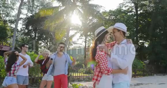 情侣在热带棕榈树公园拥抱亲吻人群欢度佳节视频的预览图