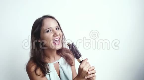 年轻漂亮的黑发微笑的女人一边唱着歌一边在白色的背景上拿着梳子慢动作3840x2160视频的预览图