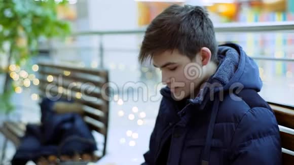 商场里的一个人坐在长凳上一个穿着蓝色夹克衫手里拿着手机的年轻人坐在长凳上视频的预览图