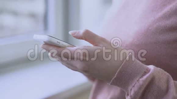 孕妇站在窗边手里拿着智能手机和滚动屏幕视频的预览图