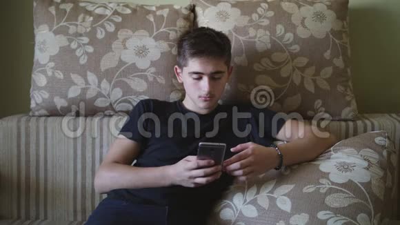 年轻的白种人在现代工业住宅中使用智能手机在沙发上放松室内视频的预览图