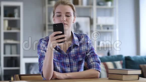 年轻女子一边在椅子上休息一边忙着用智能手机视频的预览图