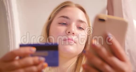 一个穿着黄色毛衣的金发女孩正在房间里坐着电话背景是粉红色的窗帘和视频的预览图