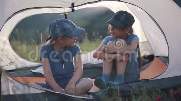 孩子们在户外坐在帐篷里愉快地聊天两个小女孩旅行者视频的预览图