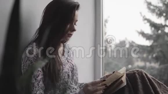 漂亮的小姐坐在房子的窗台上看书大窗户绿植视频的预览图