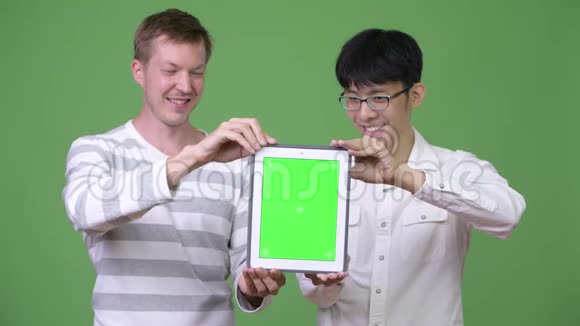 两个快乐的年轻多民族商人一起向摄像机展示数字平板电脑视频的预览图