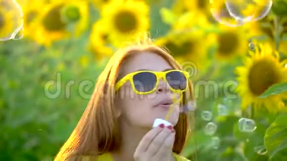 红长发的美女站在黄色的向日葵地上吹泡泡快乐的女人在户外青少年视频的预览图