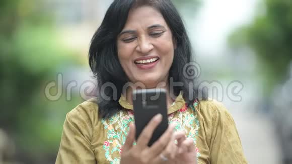 成熟快乐美丽的印度女人在户外的街道上使用电话视频的预览图